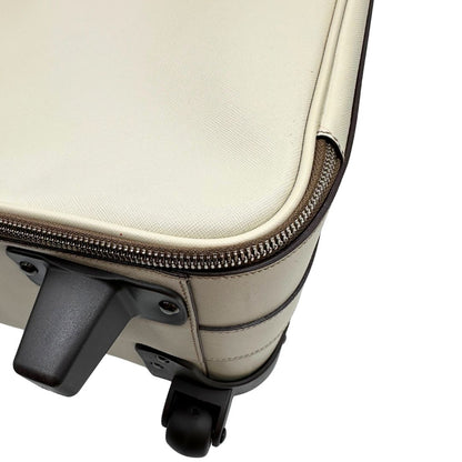 Appoggio di una valigia Prada in pelle saffiano bianco latte e finiture nere, con dettagli metallici argentati. L’interno è foderato in tessuto jacquard con motivo logo Prada, dotato di cinghie regolabili per fissare il contenuto e tasca con zip. Dispone di doppia chiusura con cerniera e lucchetto numerico in metallo argentato, manico superiore e laterale in pelle, maniglia estraibile e ruote posteriori per facilitarne il trasporto. Completa di dustbag, clochette porta address e card d'autenticità.