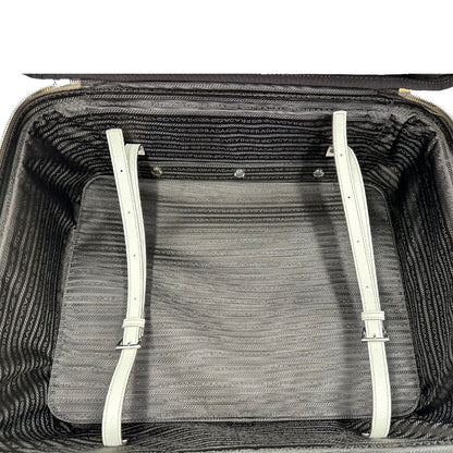 Interno di una valigia Prada in pelle saffiano bianco latte e finiture nere, con dettagli metallici argentati. L’interno è foderato in tessuto jacquard con motivo logo Prada, dotato di cinghie regolabili per fissare il contenuto e tasca con zip. Dispone di doppia chiusura con cerniera e lucchetto numerico in metallo argentato, manico superiore e laterale in pelle, maniglia estraibile e ruote posteriori per facilitarne il trasporto. Completa di dustbag, clochette porta address e card d'autenticità.