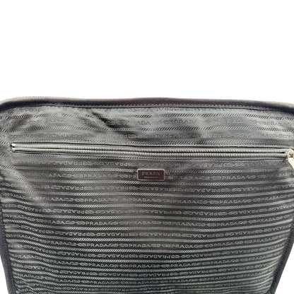 Interno di una valigia Prada in pelle saffiano bianco latte e finiture nere, con dettagli metallici argentati. L’interno è foderato in tessuto jacquard con motivo logo Prada, dotato di cinghie regolabili per fissare il contenuto e tasca con zip. Dispone di doppia chiusura con cerniera e lucchetto numerico in metallo argentato, manico superiore e laterale in pelle, maniglia estraibile e ruote posteriori per facilitarne il trasporto. Completa di dustbag, clochette porta address e card d'autenticità.