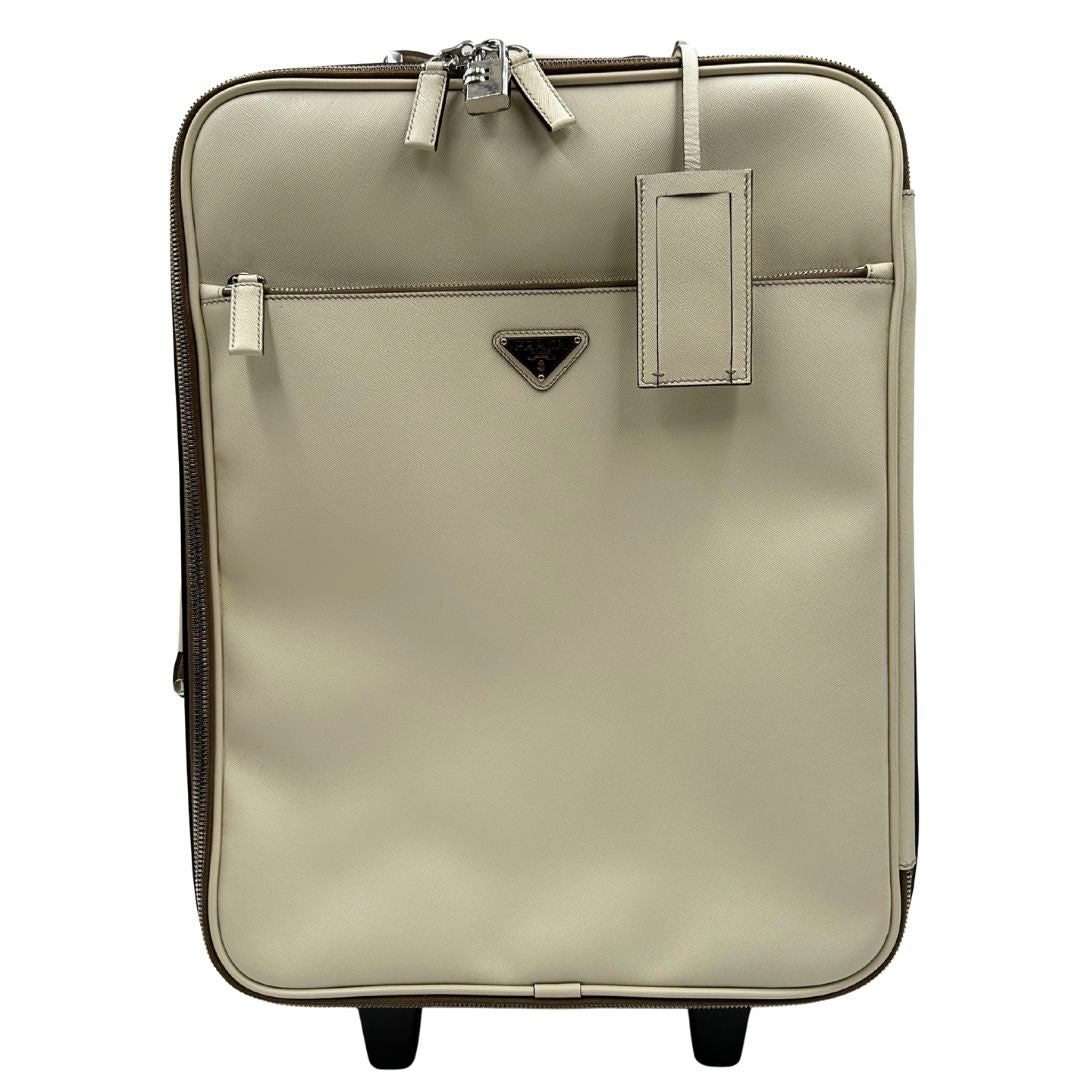 Front di una valigia Prada in pelle saffiano bianco latte e finiture nere, con dettagli metallici argentati. L’interno è foderato in tessuto jacquard con motivo logo Prada, dotato di cinghie regolabili per fissare il contenuto e tasca con zip. Dispone di doppia chiusura con cerniera e lucchetto numerico in metallo argentato, manico superiore e laterale in pelle, maniglia estraibile e ruote posteriori per facilitarne il trasporto. Completa di dustbag, clochette porta address e card d'autenticità.