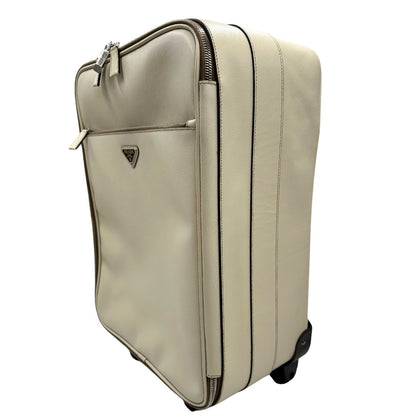 Laterale destro di una valigia Prada in pelle saffiano bianco latte e finiture nere, con dettagli metallici argentati. L’interno è foderato in tessuto jacquard con motivo logo Prada, dotato di cinghie regolabili per fissare il contenuto e tasca con zip. Dispone di doppia chiusura con cerniera e lucchetto numerico in metallo argentato, manico superiore e laterale in pelle, maniglia estraibile e ruote posteriori per facilitarne il trasporto. Completa di dustbag, clochette porta address e card d'autenticità.