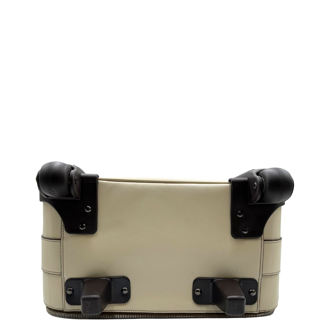 Base di una valigia Prada in pelle saffiano bianco latte e finiture nere, con dettagli metallici argentati. L’interno è foderato in tessuto jacquard con motivo logo Prada, dotato di cinghie regolabili per fissare il contenuto e tasca con zip. Dispone di doppia chiusura con cerniera e lucchetto numerico in metallo argentato, manico superiore e laterale in pelle, maniglia estraibile e ruote posteriori per facilitarne il trasporto. Completa di dustbag, clochette porta address e card d'autenticità.