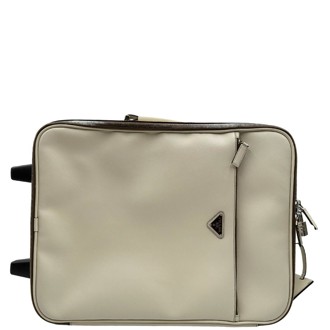 Vista superiore di una valigia Prada in pelle saffiano bianco latte e finiture nere, con dettagli metallici argentati. L’interno è foderato in tessuto jacquard con motivo logo Prada, dotato di cinghie regolabili per fissare il contenuto e tasca con zip. Dispone di doppia chiusura con cerniera e lucchetto numerico in metallo argentato, manico superiore e laterale in pelle, maniglia estraibile e ruote posteriori per facilitarne il trasporto. Completa di dustbag, clochette porta address e card d'autenticità.