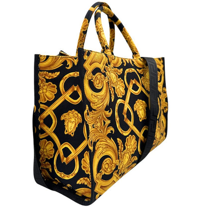 Laterale sinistro di una borsa Versace in tela com motivo jacquard barocco in nero e giallo tipico della Maison. Presenta doppi manici stondati e una tracolla amovibile in tessuto motivo greca, con dettagli in pelle neri. Completa di dustbag.