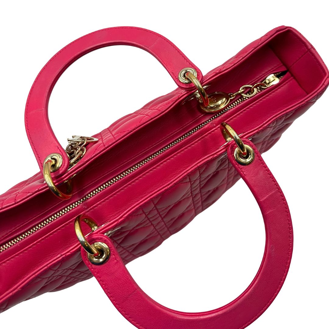 Vista superiore di una borsa Lady Dior Large in pelle fucsia in trama cannage. Doppi manici rigidi, con parti metalliche dorate. Completa di dustbag. Indossabile a mano.
