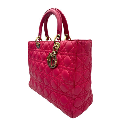 Laterale destro di una borsa Lady Dior Large in pelle fucsia in trama cannage. Doppi manici rigidi, con parti metalliche dorate. Completa di dustbag. Indossabile a mano.