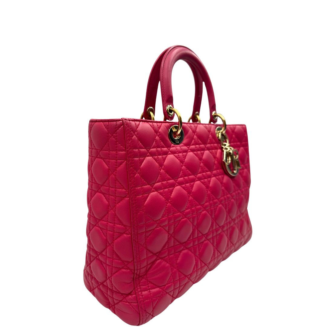 Laterale sinistro di una borsa Lady Dior Large in pelle fucsia in trama cannage. Doppi manici rigidi, con parti metalliche dorate. Completa di dustbag. Indossabile a mano.