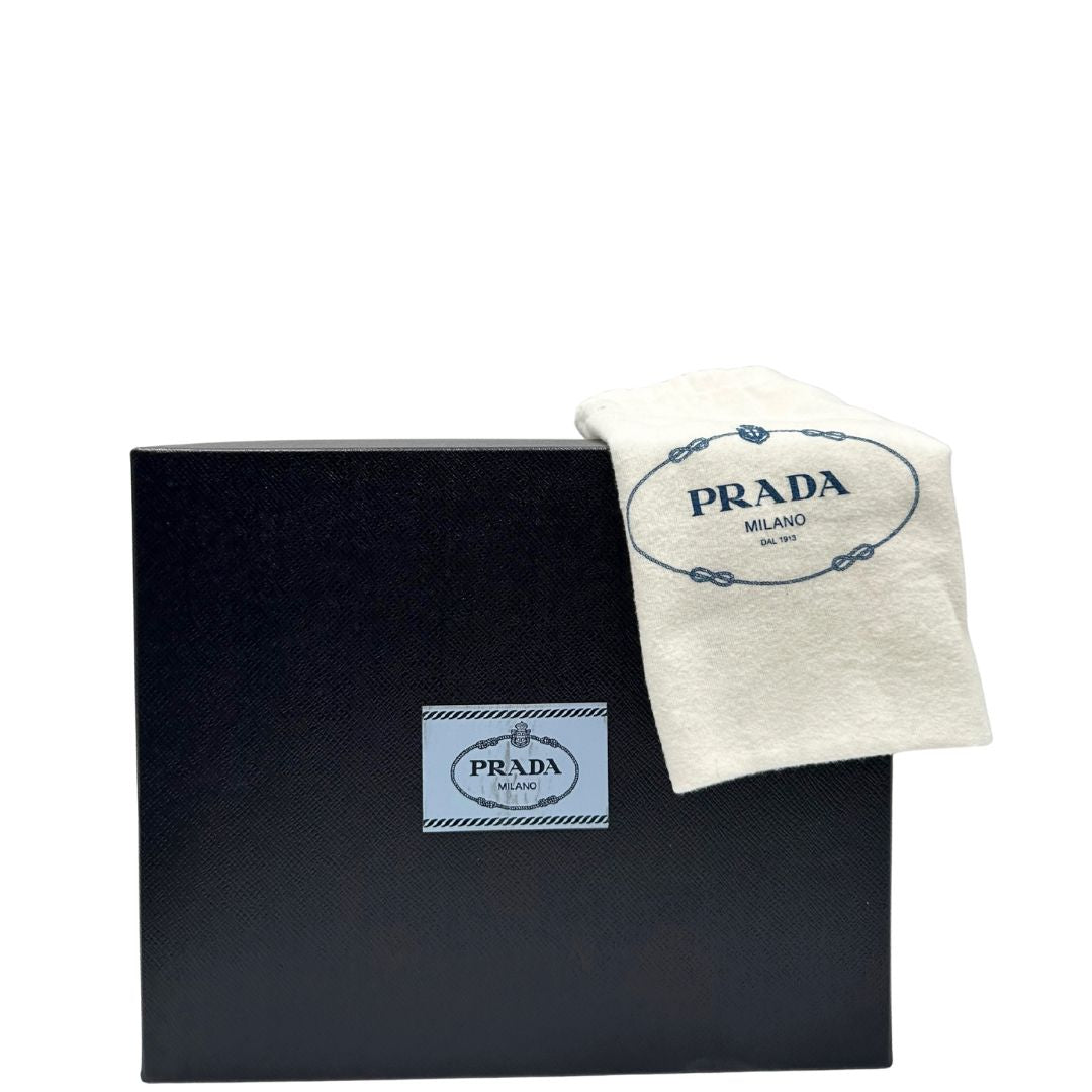 scatola e dustbag di una borsa Prada in pelle saffiano nera, con parti metalliche dorate. Dotata di una tracolla in tessuto regolabile ed amovibile, con pouch porta monete removibile e di una tracollina in catena. Munita di clochette porta chiavi. Indossabile a spalla o a tracolla.
