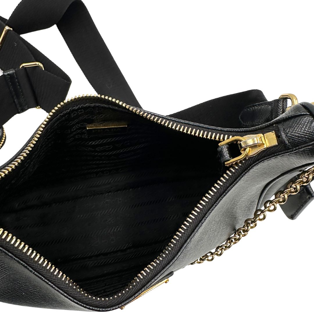 Interno di una borsa Prada in pelle saffiano nera, con parti metalliche dorate. Dotata di una tracolla in tessuto regolabile ed amovibile, con pouch porta monete removibile e di una tracollina in catena. Munita di clochette porta chiavi. Indossabile a spalla o a tracolla. Full set.