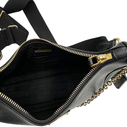 Interno di una borsa Prada in pelle saffiano nera, con parti metalliche dorate. Dotata di una tracolla in tessuto regolabile ed amovibile, con pouch porta monete removibile e di una tracollina in catena. Munita di clochette porta chiavi. Indossabile a spalla o a tracolla. Full set.