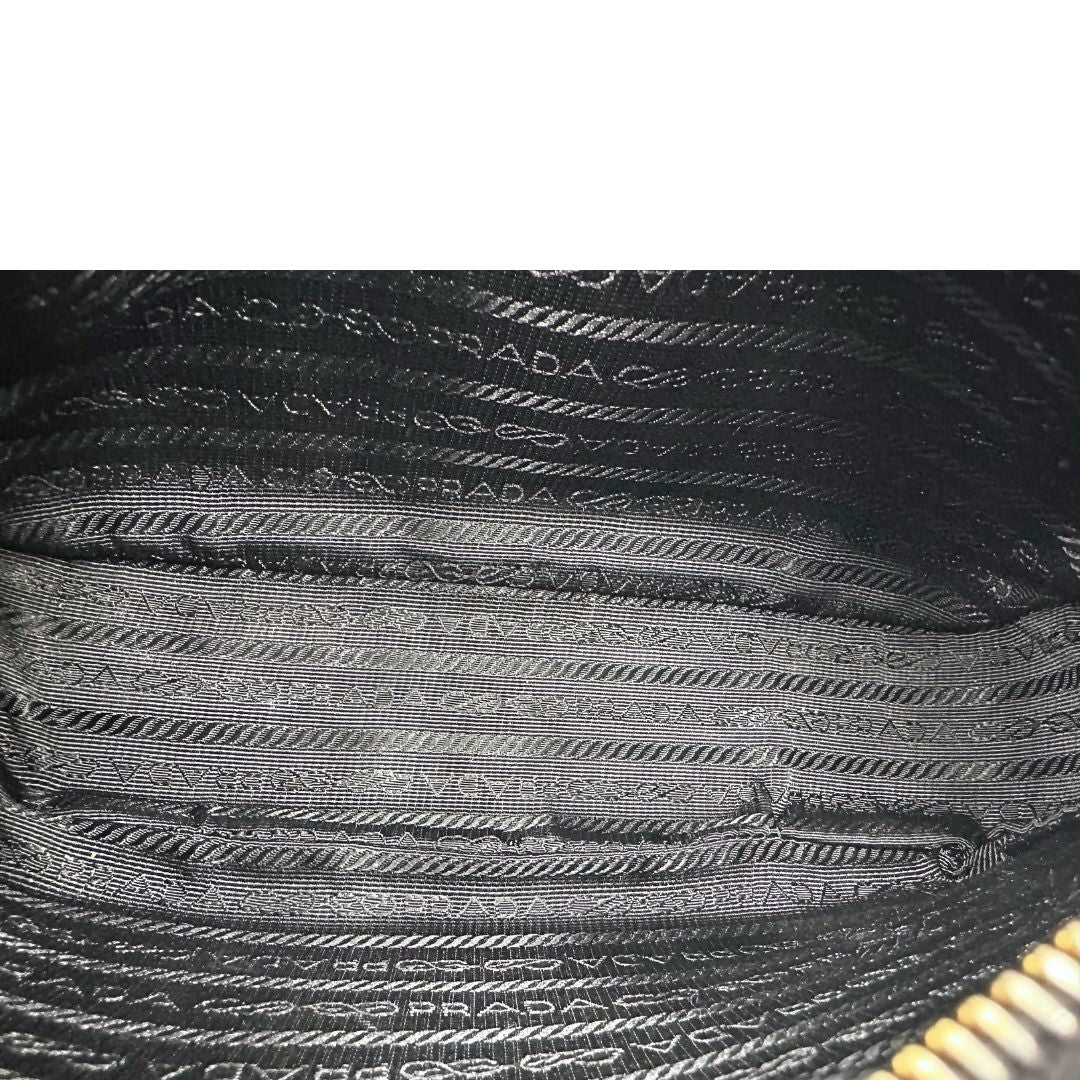 Interno di una borsa Prada in pelle saffiano nera, con parti metalliche dorate. Dotata di una tracolla in tessuto regolabile ed amovibile, con pouch porta monete removibile e di una tracollina in catena. Munita di clochette porta chiavi. Indossabile a spalla o a tracolla. Full set.