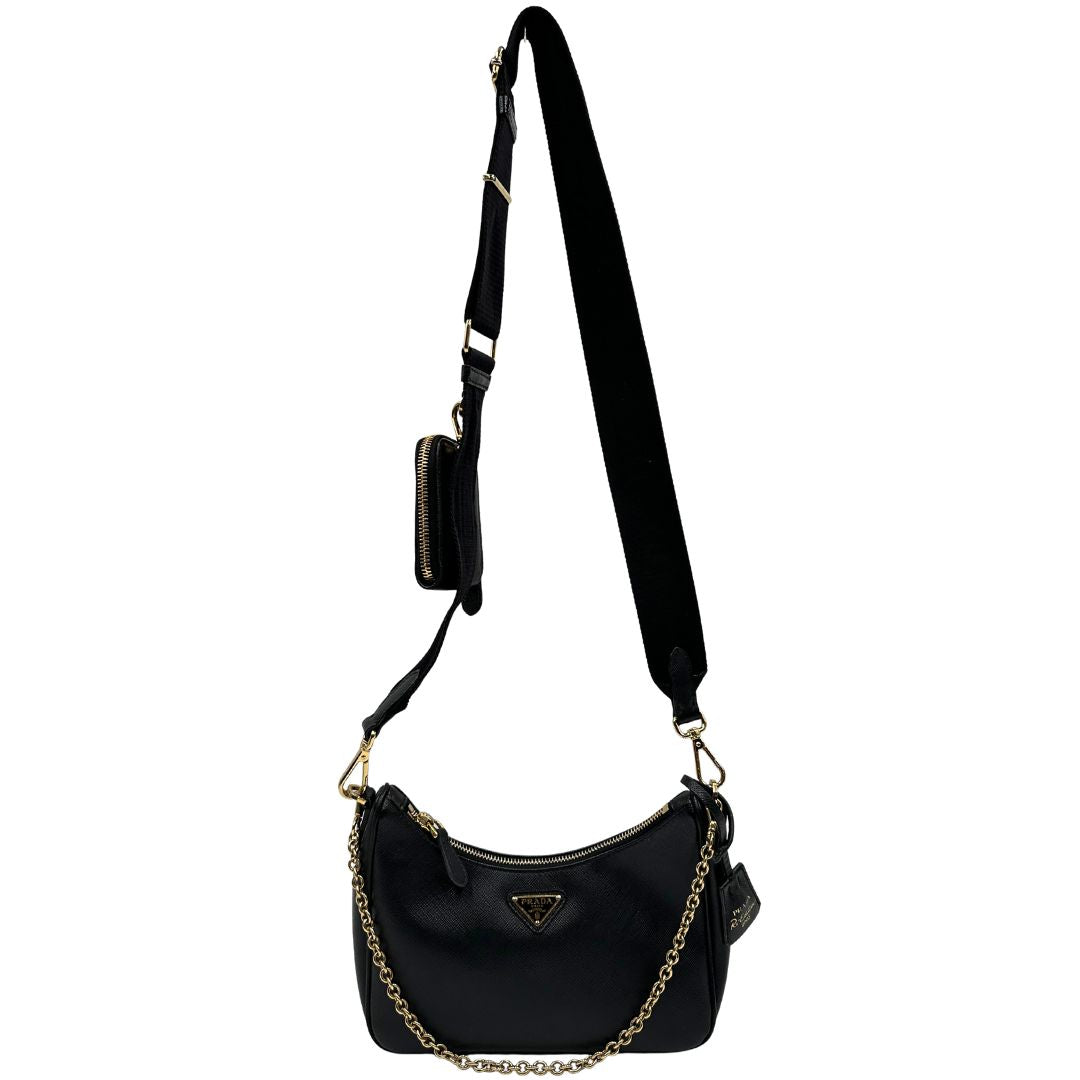 Front di una borsa Prada in pelle saffiano nera, con parti metalliche dorate. Dotata di una tracolla in tessuto regolabile ed amovibile, con pouch porta monete removibile e di una tracollina in catena. Munita di clochette porta chiavi. Indossabile a spalla o a tracolla. Full set.