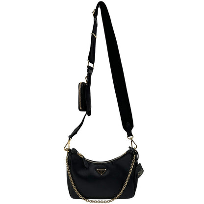 Front di una borsa Prada in pelle saffiano nera, con parti metalliche dorate. Dotata di una tracolla in tessuto regolabile ed amovibile, con pouch porta monete removibile e di una tracollina in catena. Munita di clochette porta chiavi. Indossabile a spalla o a tracolla. Full set.