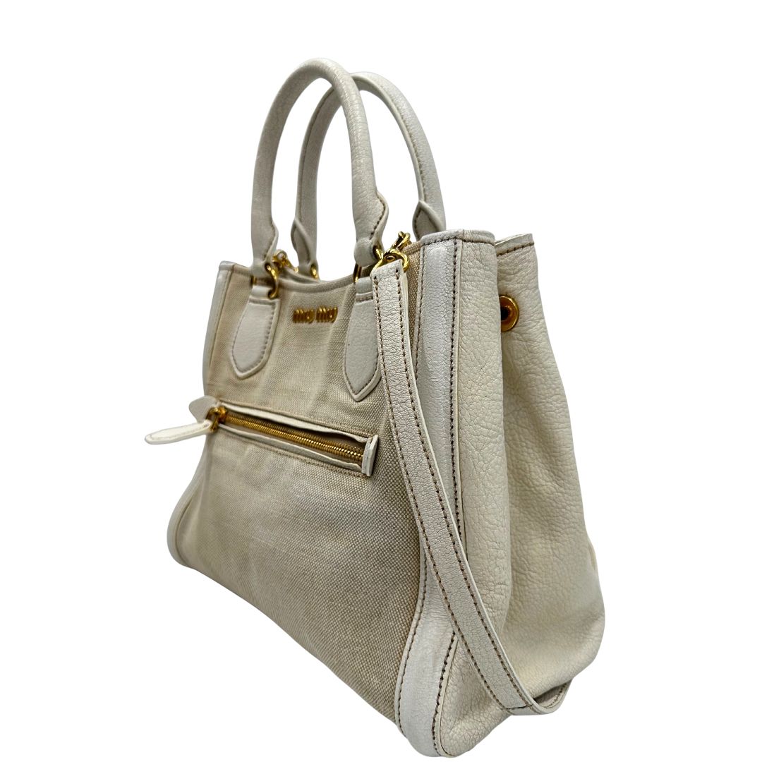 Laterale destro di una borsa Miu Miu in misto lino avorio con finiture in pelle color bianco latte e parti metalliche dorate; munita di doppi manici stondati ed una tracolla amovibile e regolabile. Completa di card d'autenticità. Indossabile a mano e a tracolla.
