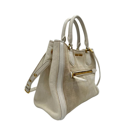 Laterale sinistro di una borsa Miu Miu in misto lino avorio con finiture in pelle color bianco latte e parti metalliche dorate; munita di doppi manici stondati ed una tracolla amovibile e regolabile. Completa di card d'autenticità. Indossabile a mano e a tracolla.