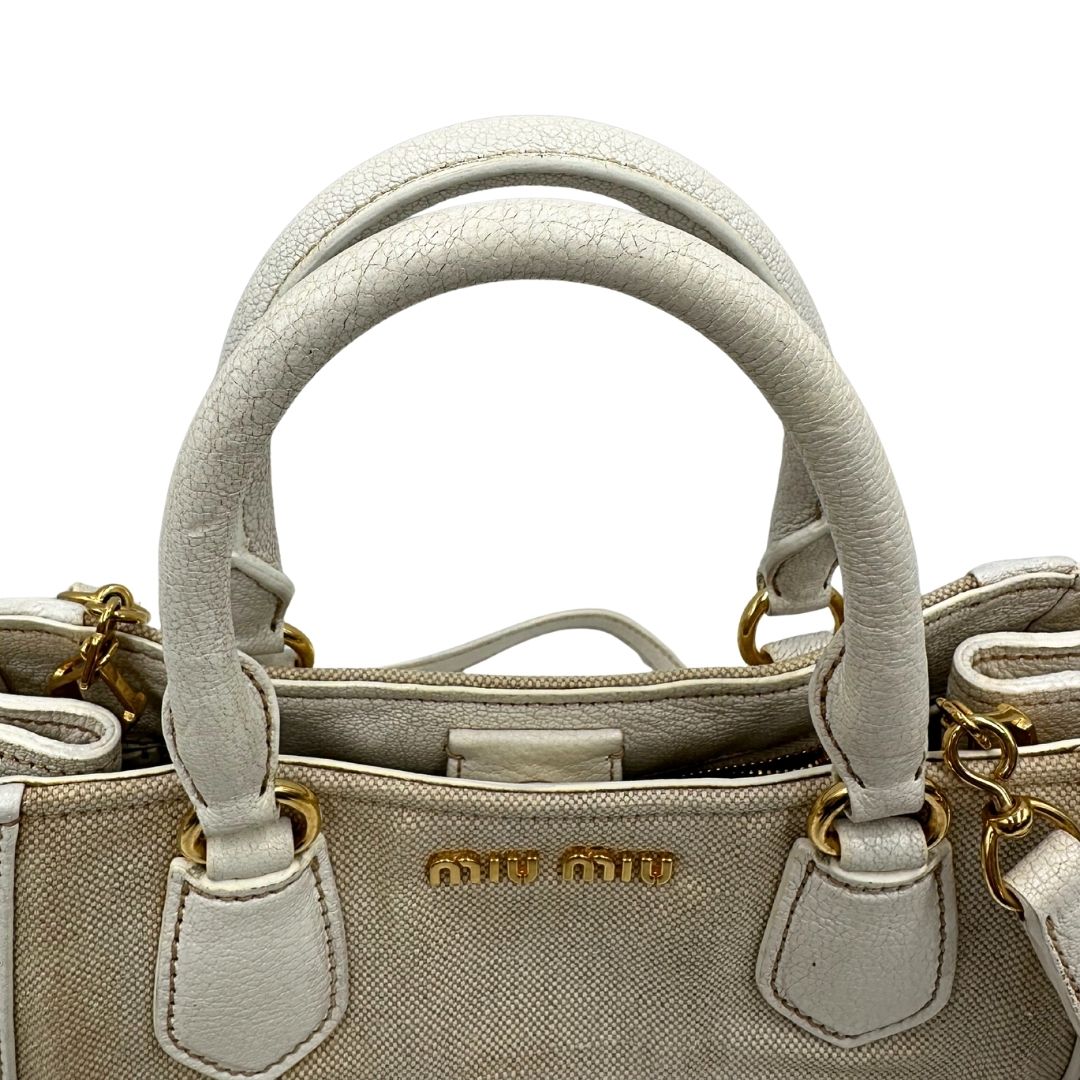 Manici di una borsa Miu Miu in misto lino avorio con finiture in pelle color bianco latte e parti metalliche dorate; munita di doppi manici stondati ed una tracolla amovibile e regolabile. Completa di card d'autenticità. Indossabile a mano e a tracolla.