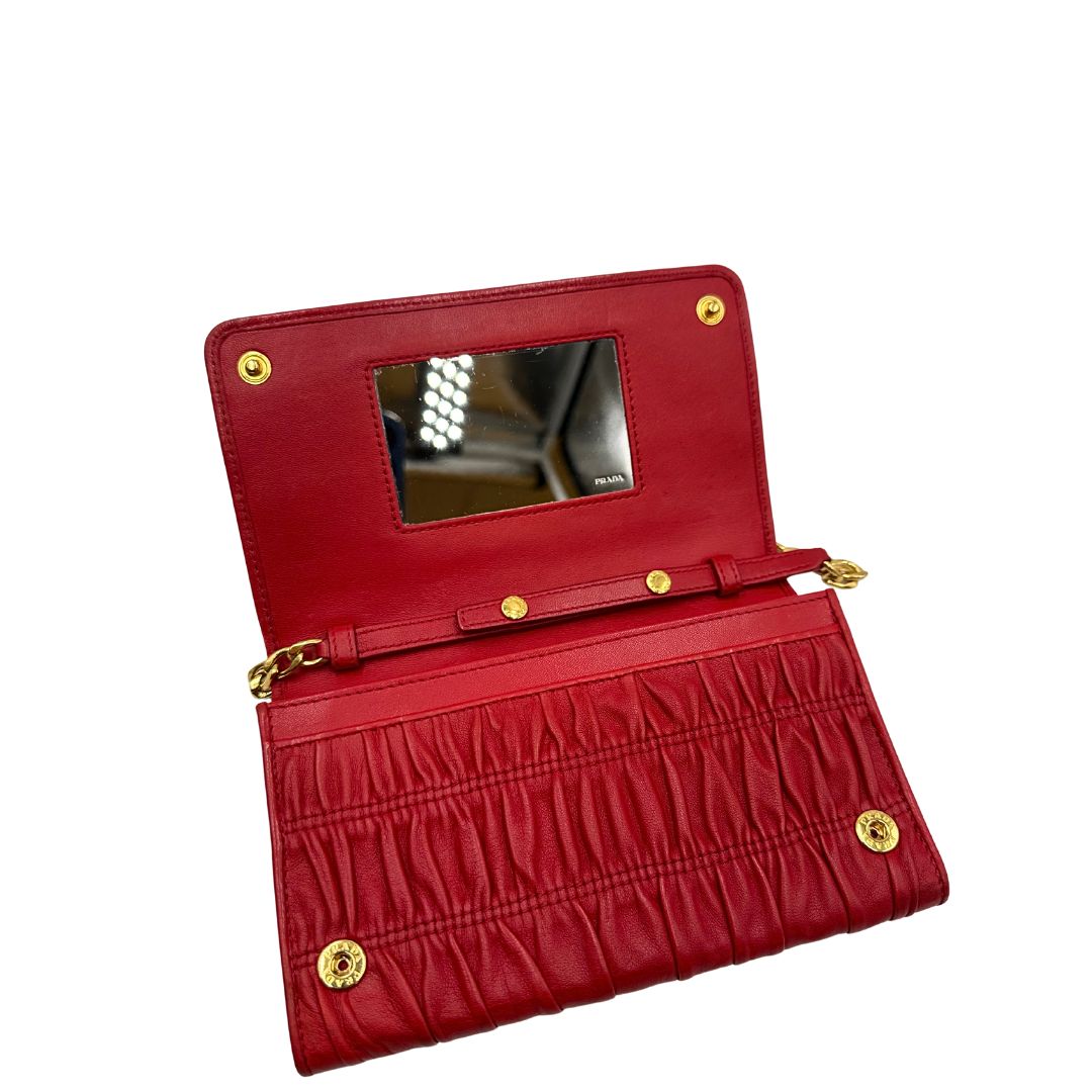 Interno di un wallet Prada in pelle goffrata rossa, impreziosito da logo lettering sul front e specchietto interno; munito di una tracolla in catena amovibile e non regolabile. Completo di scatola.