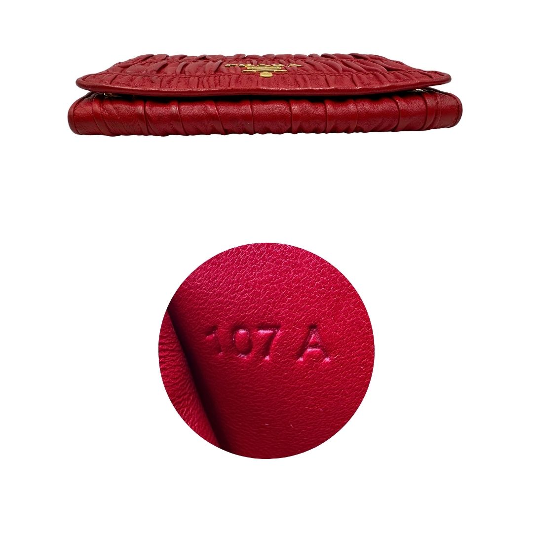 Base e codice di un wallet Prada in pelle goffrata rossa, impreziosito da logo lettering sul front e specchietto interno; munito di una tracolla in catena amovibile e non regolabile. Completo di scatola.