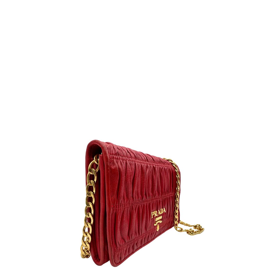 Laterale sinistro di un wallet Prada in pelle goffrata rossa, impreziosito da logo lettering sul front e specchietto interno; munito di una tracolla in catena amovibile e non regolabile. Completo di scatola.