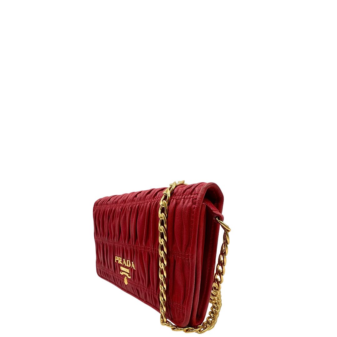 Laterale destro di un wallet Prada in pelle goffrata rossa, impreziosito da logo lettering sul front e specchietto interno; munito di una tracolla in catena amovibile e non regolabile. Completo di scatola.