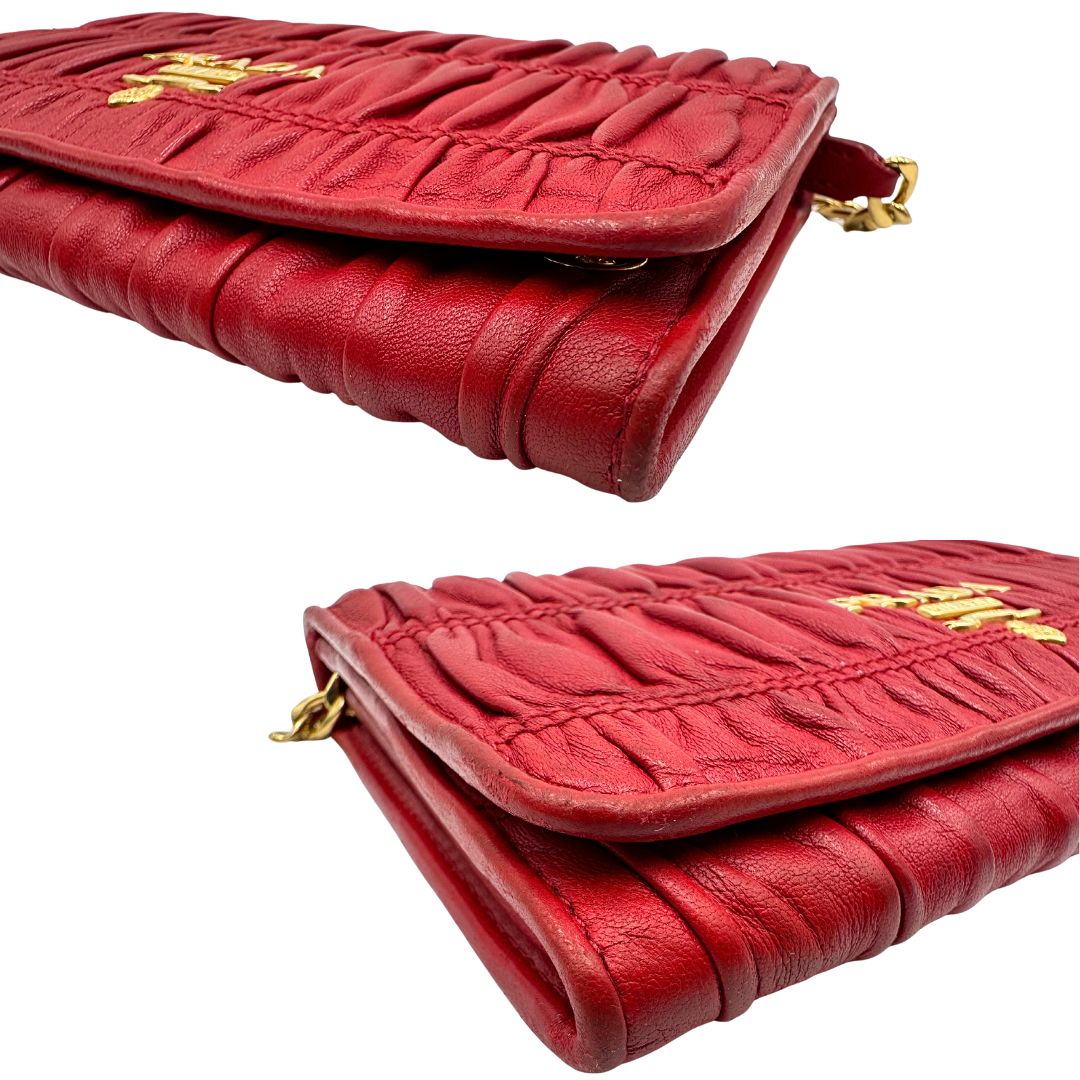 Angoli di un wallet Prada in pelle goffrata rossa, impreziosito da logo lettering sul front e specchietto interno; munito di una tracolla in catena amovibile e non regolabile. Completo di scatola.