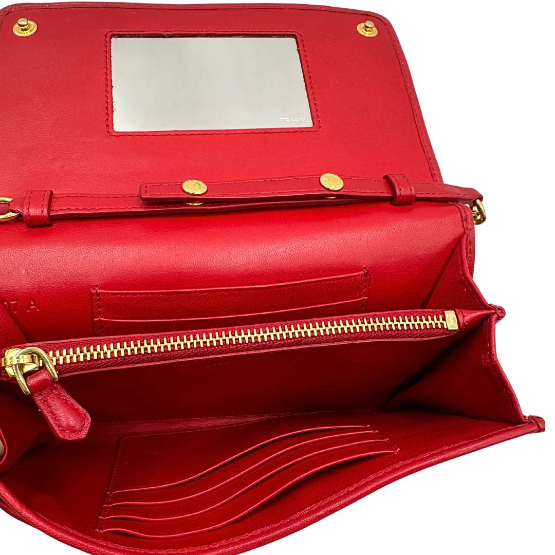 Interno di un wallet Prada in pelle goffrata rossa, impreziosito da logo lettering sul front e specchietto interno; munito di una tracolla in catena amovibile e non regolabile. Completo di scatola.
