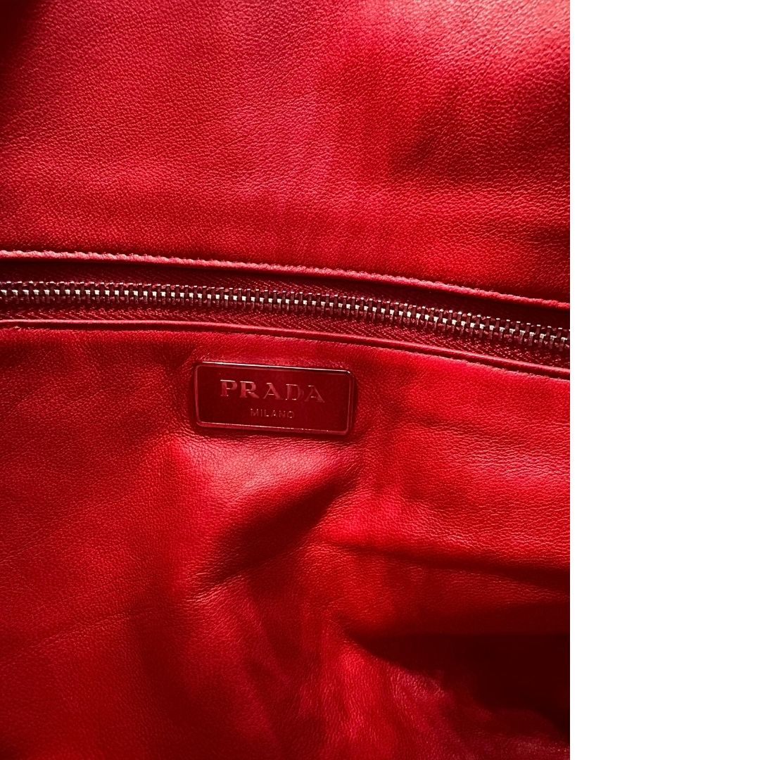 Interno di una borsa a tracolla Prada in pelle rossa, munita di una tracolla in catena e pelle amovibile e regolabile. Completa di scatola.