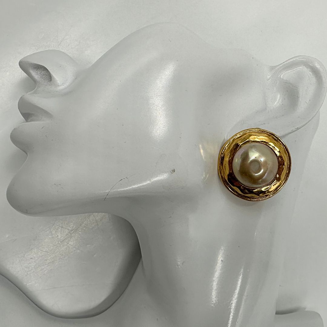 Orecchini Chanel vintage a clip, caratterizzati da una montatura in metallo dorato martellata che incornicia una grande perla artificiale centrale dal finish iridescente. Completi di scatola.