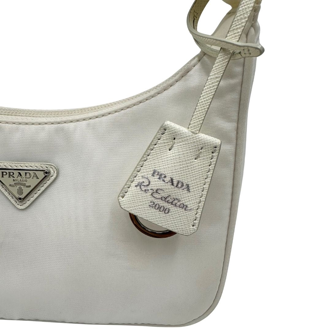Dettaglio clochette di una borsa Prada Re-Edition 2000 in econylon color bianco gesso con dettagli in pelle Saffiano tono su tono e parti metalliche argentate. Completa di corredo.