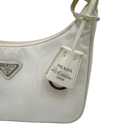 Dettaglio clochette di una borsa Prada Re-Edition 2000 in econylon color bianco gesso con dettagli in pelle Saffiano tono su tono e parti metalliche argentate. Completa di corredo.