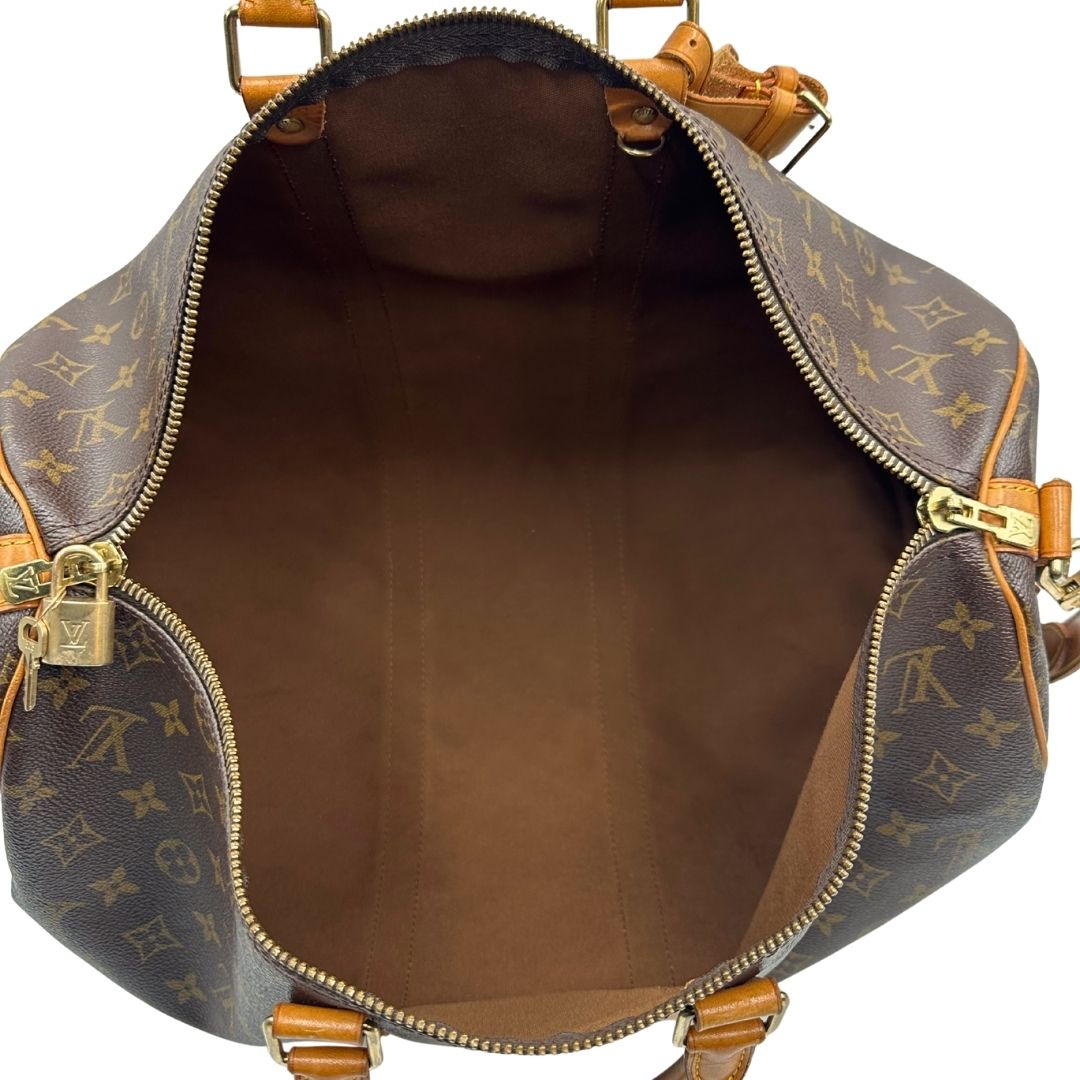 Interno di un Keepall Bandoulière in canvas monogram con finiture in vacchetta naturale e parti metalliche dorate; munito di doppi manici stondati e una tracolla amovibile e regolabile on spallaccio. Completo di lucchetto con chiave, tag porta address e ferma manici.