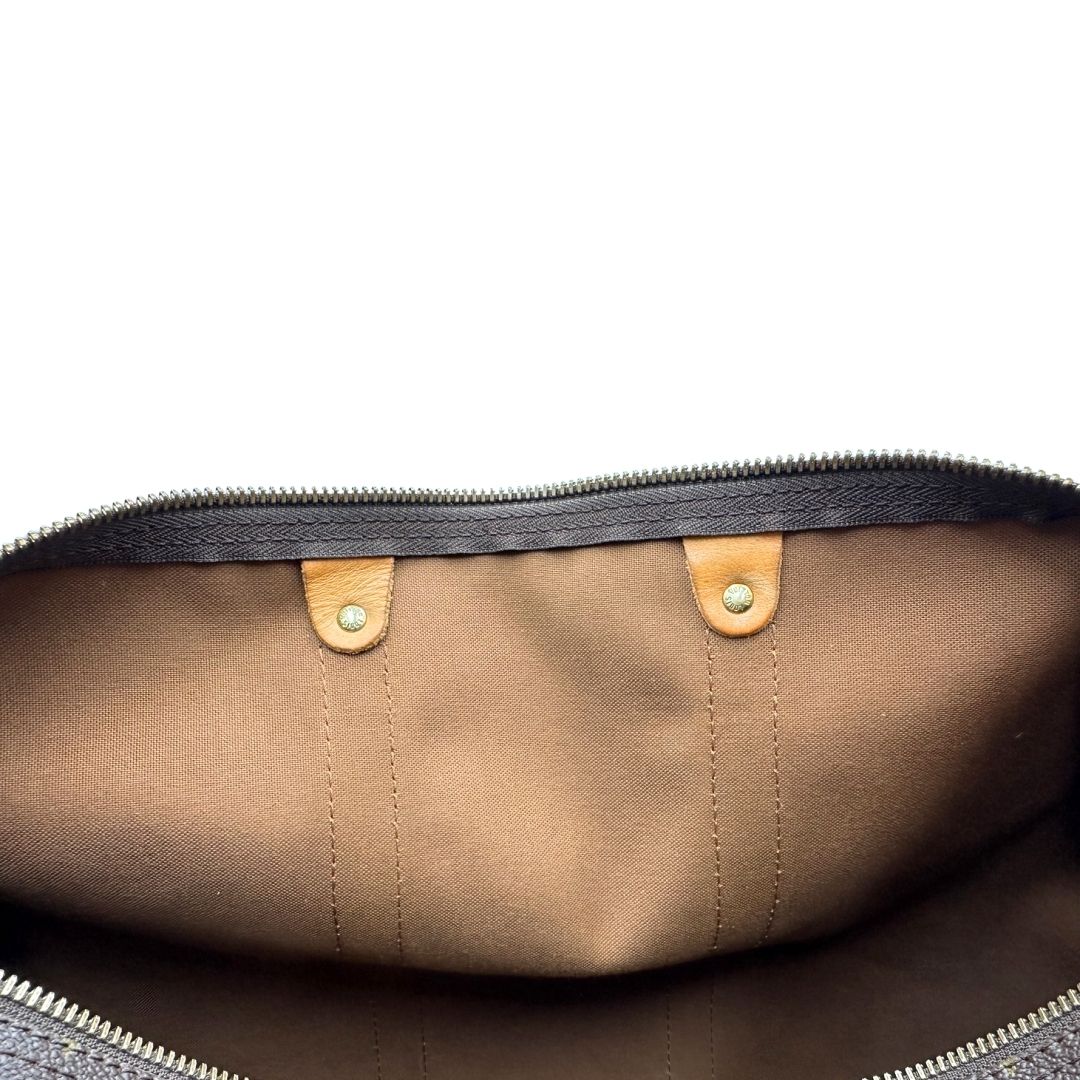 Interno di un Keepall Bandoulière in canvas monogram con finiture in vacchetta naturale e parti metalliche dorate; munito di doppi manici stondati e una tracolla amovibile e regolabile on spallaccio. Completo di lucchetto con chiave, tag porta address e ferma manici.