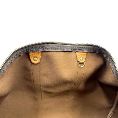 Interno di un Keepall Bandoulière in canvas monogram con finiture in vacchetta naturale e parti metalliche dorate; munito di doppi manici stondati e una tracolla amovibile e regolabile on spallaccio. Completo di lucchetto con chiave, tag porta address e ferma manici.