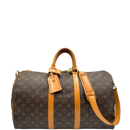 Front di un Keepall Bandoulière in canvas monogram con finiture in vacchetta naturale e parti metalliche dorate; munito di doppi manici stondati e una tracolla amovibile e regolabile on spallaccio. Completo di lucchetto con chiave, tag porta address e ferma manici.