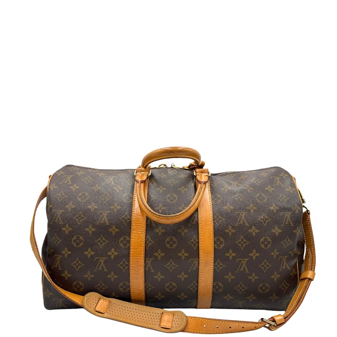 Retro di un Keepall Bandoulière in canvas monogram con finiture in vacchetta naturale e parti metalliche dorate; munito di doppi manici stondati e una tracolla amovibile e regolabile on spallaccio. Completo di lucchetto con chiave, tag porta address e ferma manici.