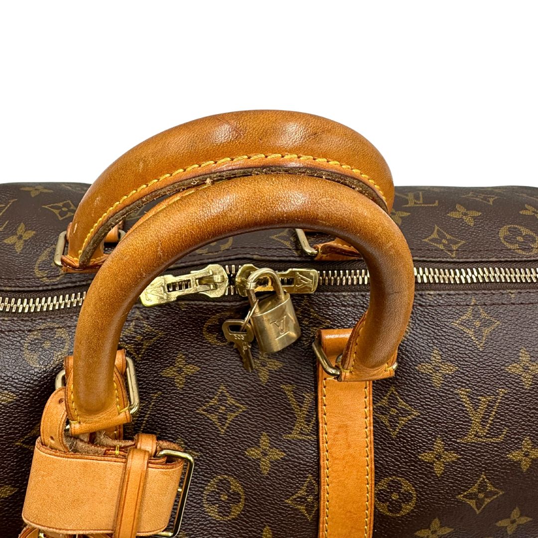 Manici di un Keepall Bandoulière in canvas monogram con finiture in vacchetta naturale e parti metalliche dorate; munito di doppi manici stondati e una tracolla amovibile e regolabile on spallaccio. Completo di lucchetto con chiave, tag porta address e ferma manici.