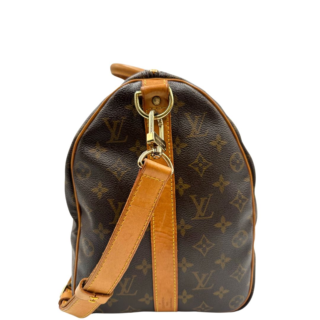 Vista laterale di un Keepall Bandoulière in canvas monogram con finiture in vacchetta naturale e parti metalliche dorate; munito di doppi manici stondati e una tracolla amovibile e regolabile on spallaccio. Completo di lucchetto con chiave, tag porta address e ferma manici.