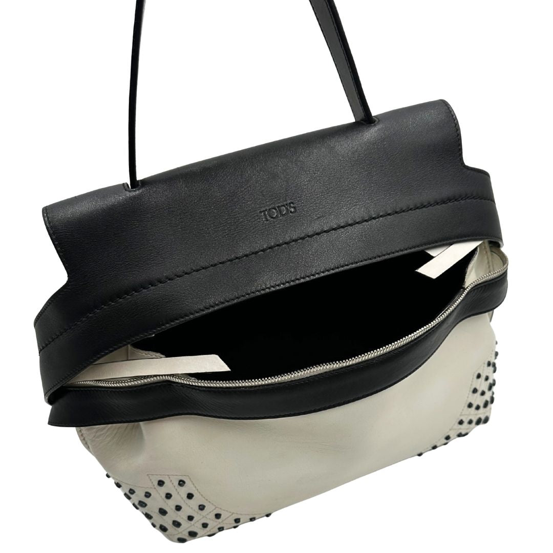 Apertura di una borsa Wave Tod's in pelle bianca e nera impreziosita da iconici gommini Tod's sugli angoli della base. Munita di un manico singolo stondato, una tracolla con lettere in catena e pelle, regolabile ed amovibile. Parti metalliche argentate. Dotata di dustbag.