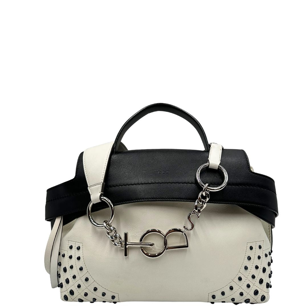 Front di una borsa Wave Tod's in pelle bianca e nera impreziosita da iconici gommini Tod's sugli angoli della base. Munita di un manico singolo stondato, una tracolla con lettere in catena e pelle, regolabile ed amovibile. Parti metalliche argentate. Dotata di dustbag.