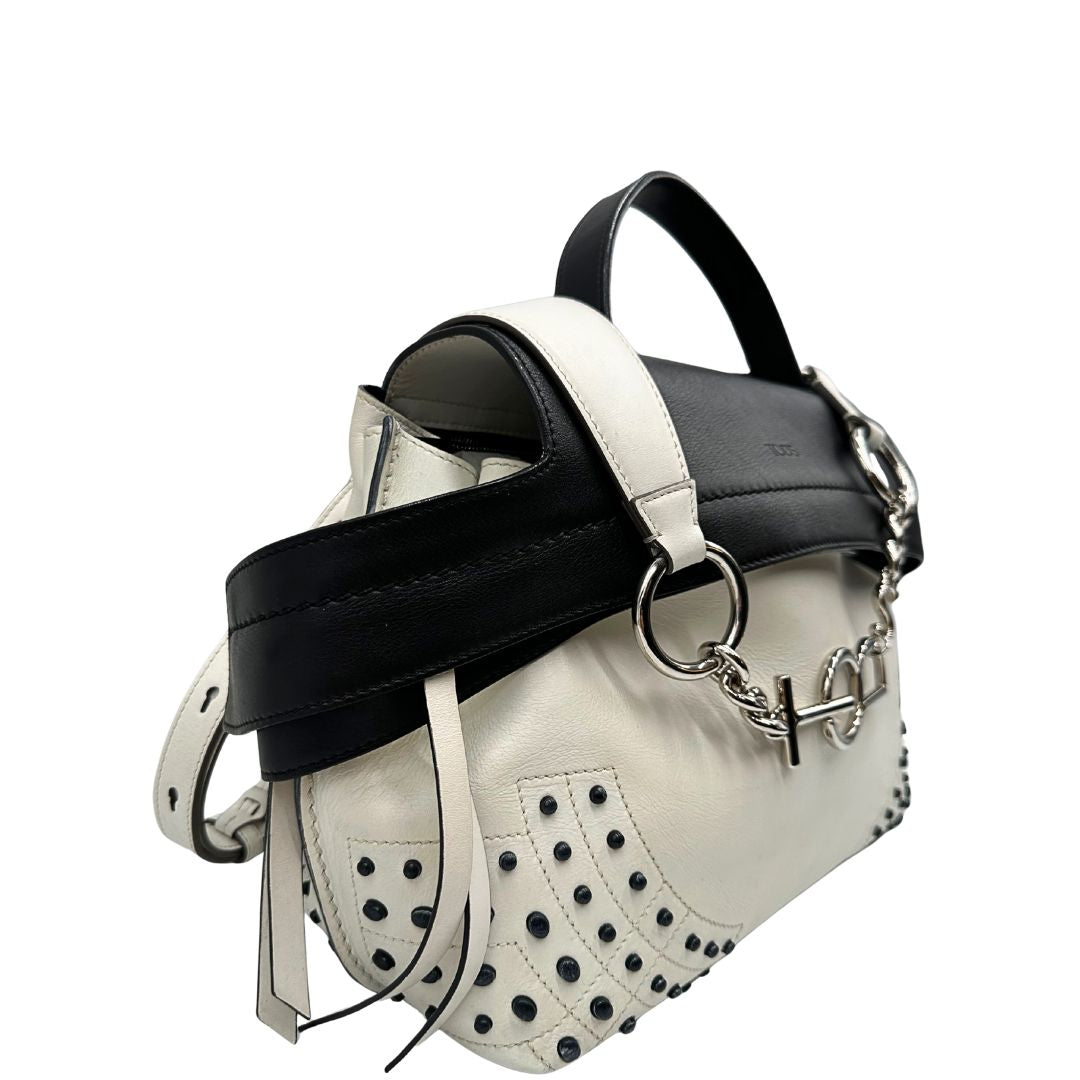 Laterale sinistro di una borsa Wave Tod's in pelle bianca e nera impreziosita da iconici gommini Tod's sugli angoli della base. Munita di un manico singolo stondato, una tracolla con lettere in catena e pelle, regolabile ed amovibile. Parti metalliche argentate. Dotata di dustbag.