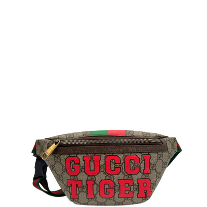 Front di un marsupio Gucci in canvas beige GG con metalleria dorata e finiture in pelle marroni. Stampa Gucci Tiger e fascia Web su front e retro. Tracolla in tessuto Web verde/rosso, regolabile. Completo di dustbag. Indossabile a marsupio o crossbody.