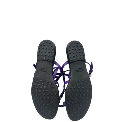 Suola di sandali Tod’s in pelle viola con fasce incrociate e borchie metalliche argentate. Presentano una chiusura con cinturino e la suola con i classici gommini in gomma. Completi di scatola e dustbag.