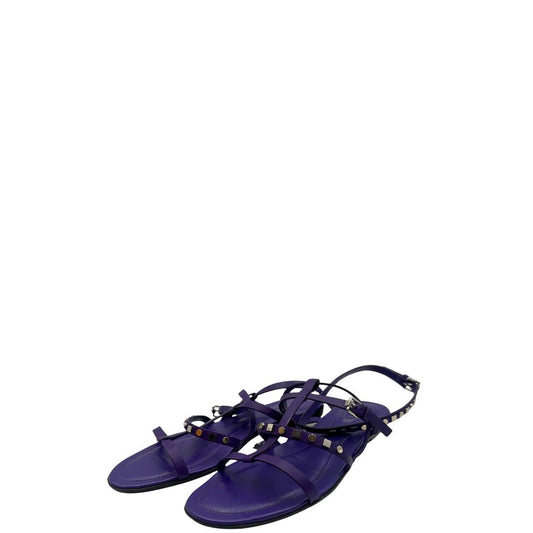 Sandali Tod’s in pelle viola con fasce incrociate e borchie metalliche argentate. Presentano una chiusura con cinturino e la suola con i classici gommini in gomma. Completi di scatola e dustbag.