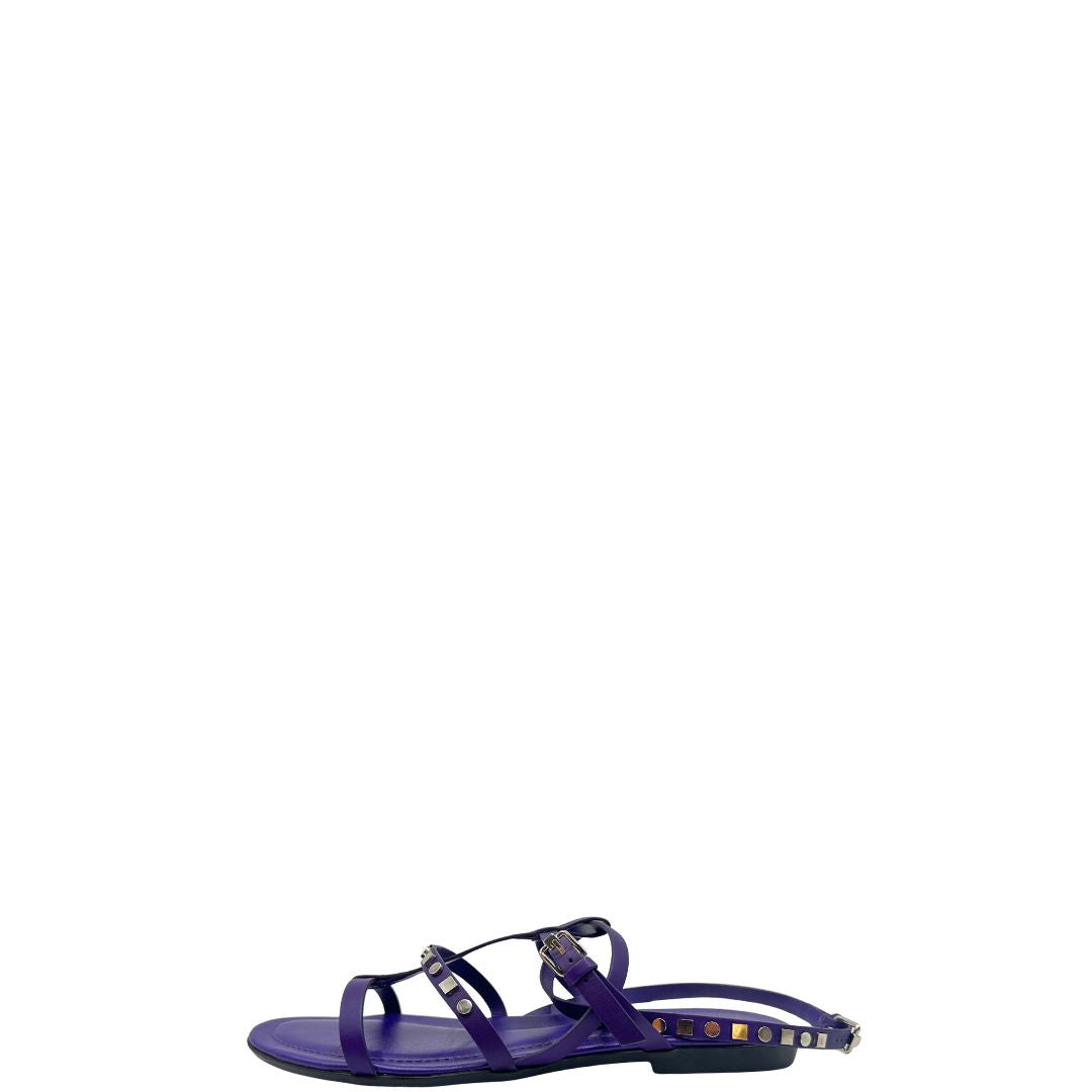 Sandali Tod’s in pelle viola con fasce incrociate e borchie metalliche argentate. Presentano una chiusura con cinturino e la suola con i classici gommini in gomma. Completi di scatola e dustbag.