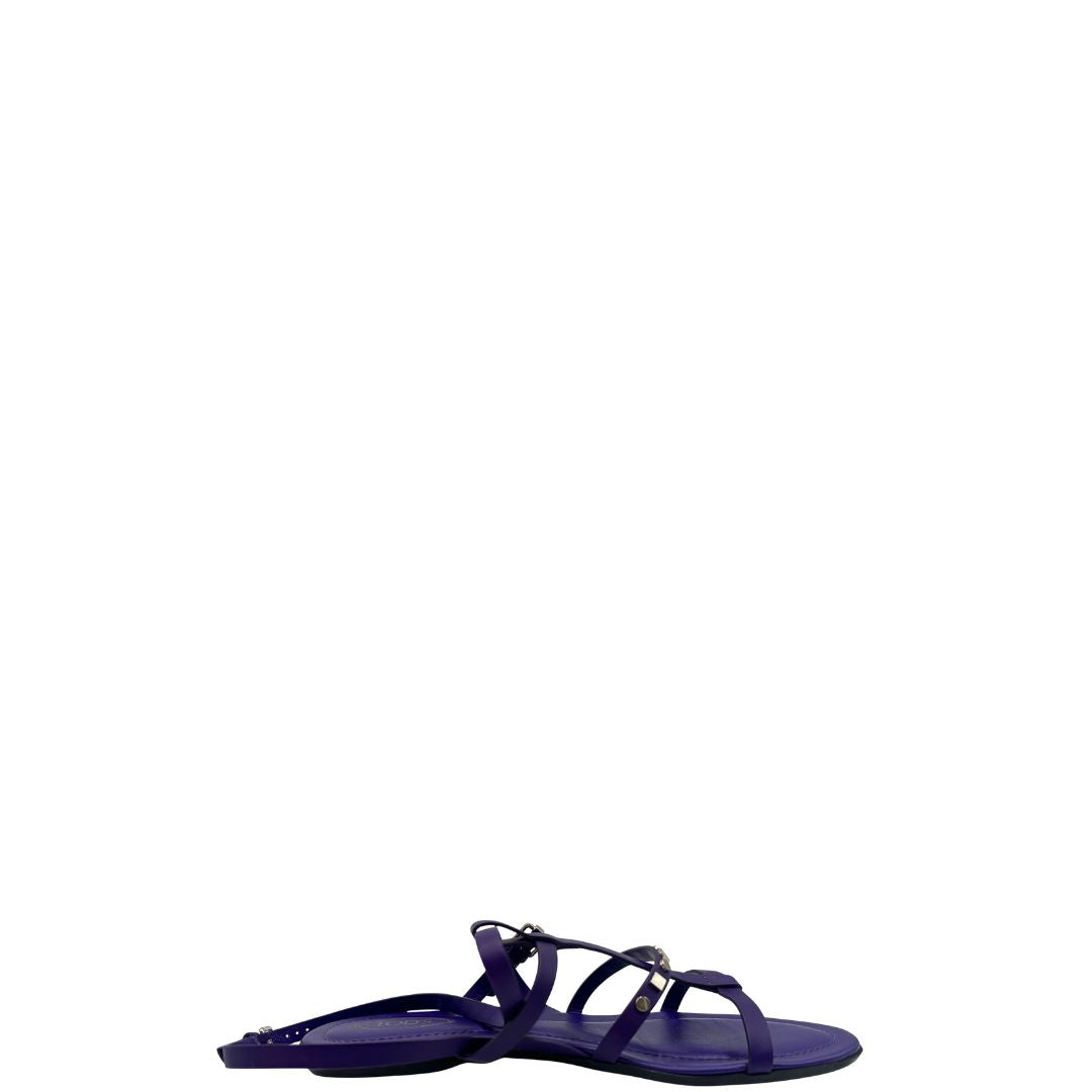 Sandali Tod’s in pelle viola con fasce incrociate e borchie metalliche argentate. Presentano una chiusura con cinturino e la suola con i classici gommini in gomma. Completi di scatola e dustbag.