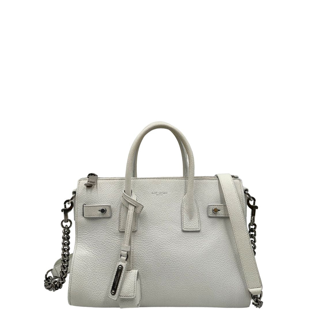 Front di una Sac De Jour small Saint Laurent in pelle martellata bianco gesso con doppi manici stondati e tracolla in catena e pelle, regolabile ed amovibile. Parti metalliche argentate. Munita di clochette con lucchetto e chiavi.