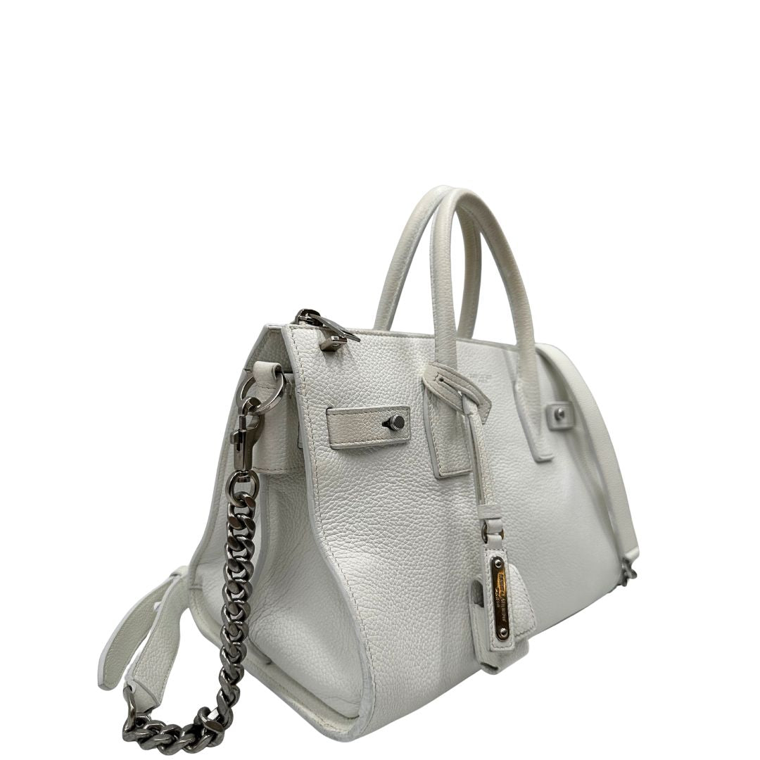 Laterale sinistro di una Sac De Jour small Saint Laurent in pelle martellata bianco gesso con doppi manici stondati e tracolla in catena e pelle, regolabile ed amovibile. Parti metalliche argentate. Munita di clochette con lucchetto e chiavi.