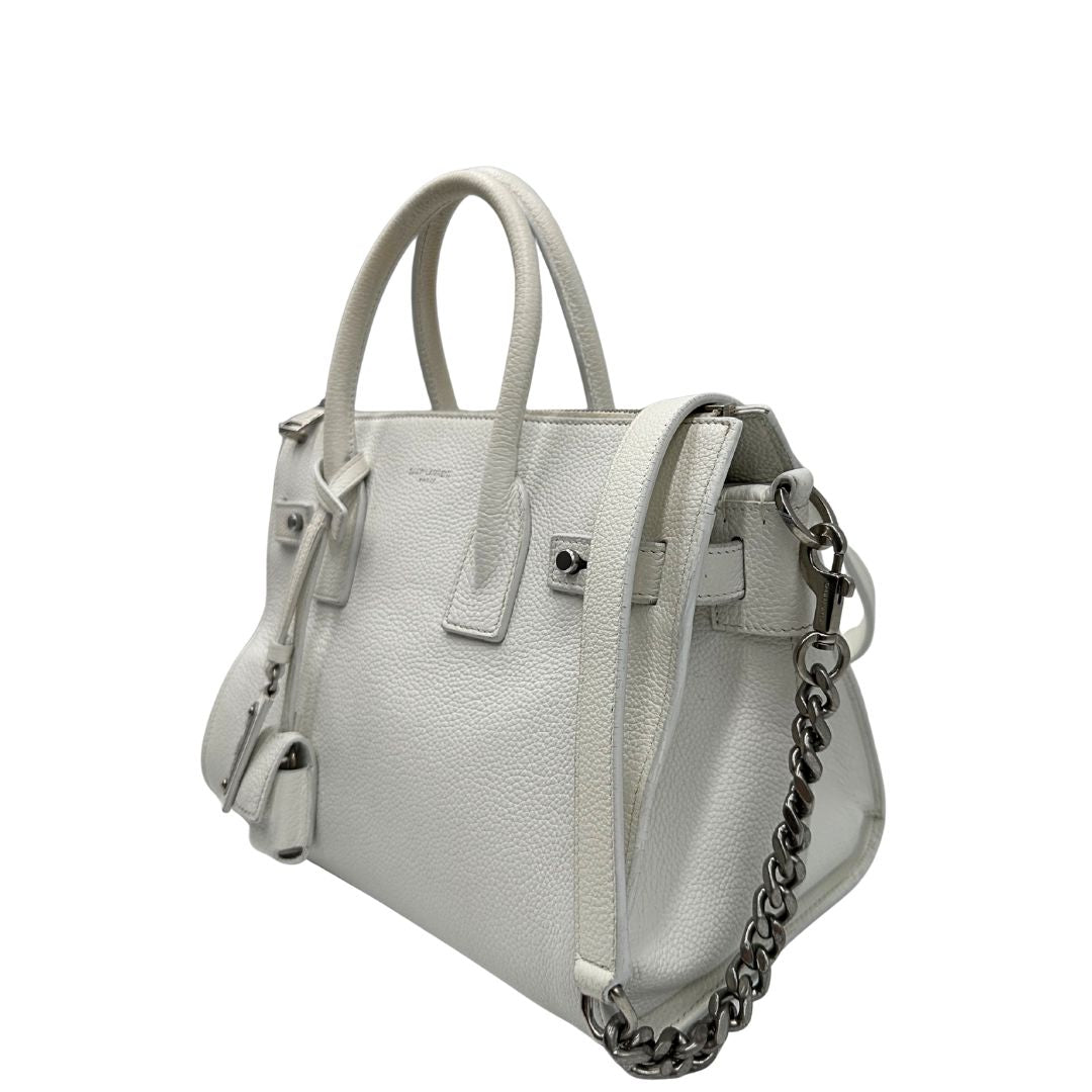 Laterale destro di una Sac De Jour small Saint Laurent in pelle martellata bianco gesso con doppi manici stondati e tracolla in catena e pelle, regolabile ed amovibile. Parti metalliche argentate. Munita di clochette con lucchetto e chiavi.