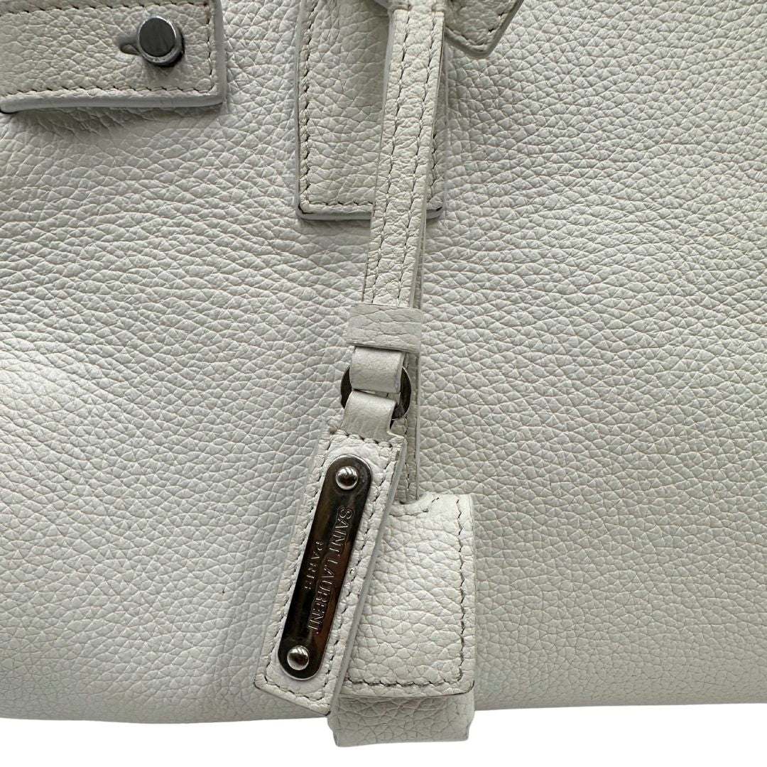 Dettagli di una Sac De Jour small Saint Laurent in pelle martellata bianco gesso con doppi manici stondati e tracolla in catena e pelle, regolabile ed amovibile. Parti metalliche argentate. Munita di clochette con lucchetto e chiavi.