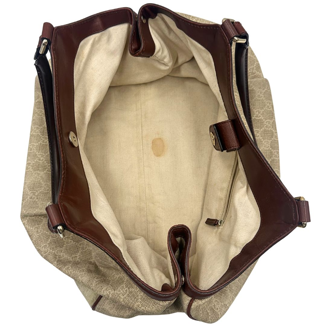 Interno di una borsa Gucci Sukey in tessuto beige GG con finiture in pelle marrone mogano, doppi manici stondati e ciondolo con doppie G incrociate. Rifinita con parti metalliche dorate. Indossabile a spalla.